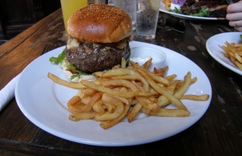 A burger and fries on a plate. This burger is probably bigger than a small child's face