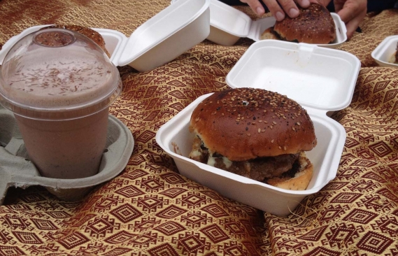 A burger in a foam box with a milkshake next to it