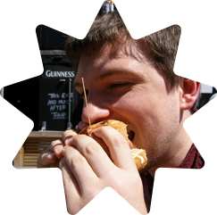 Mark tucking into a burger whilst trying to avoid having his eye poked out by a toothpick
