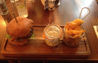 The burger, relish and chips (in a little fry basket) on a wooden plank instead of a plate