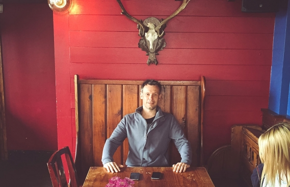 A picture of Dan under a cow's head waiting for the arrival of his tasty double cheeseburger.